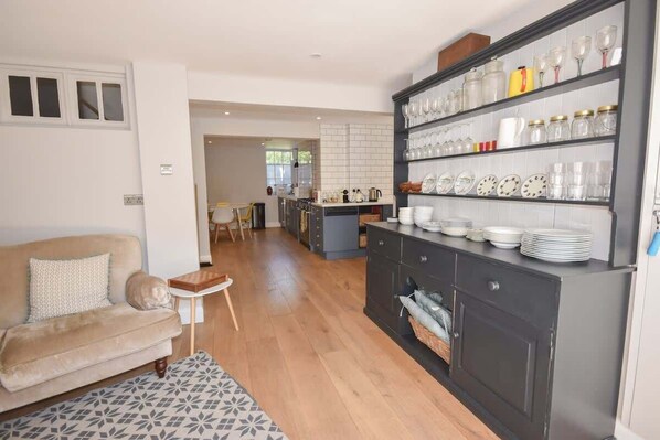 A modern kitchen with a dark cabinet, a dining area with a small table, and a living room with a sofa.
