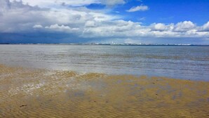 Ein Strand mit Blick auf das Meer und entfernte Gebäude.