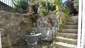 Eine Steinmauer, Außenbereich mit Stühlen und Tisch sowie eine Treppe aus Stein.