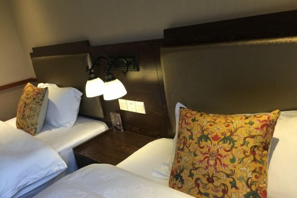 A hotel room with two beds, each with white linens and decorative pillows. There is a nightstand with a lamp between the beds.