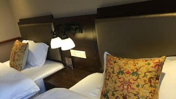 A hotel room with two beds, each with white linens and decorative pillows. There is a nightstand with a lamp between the beds.