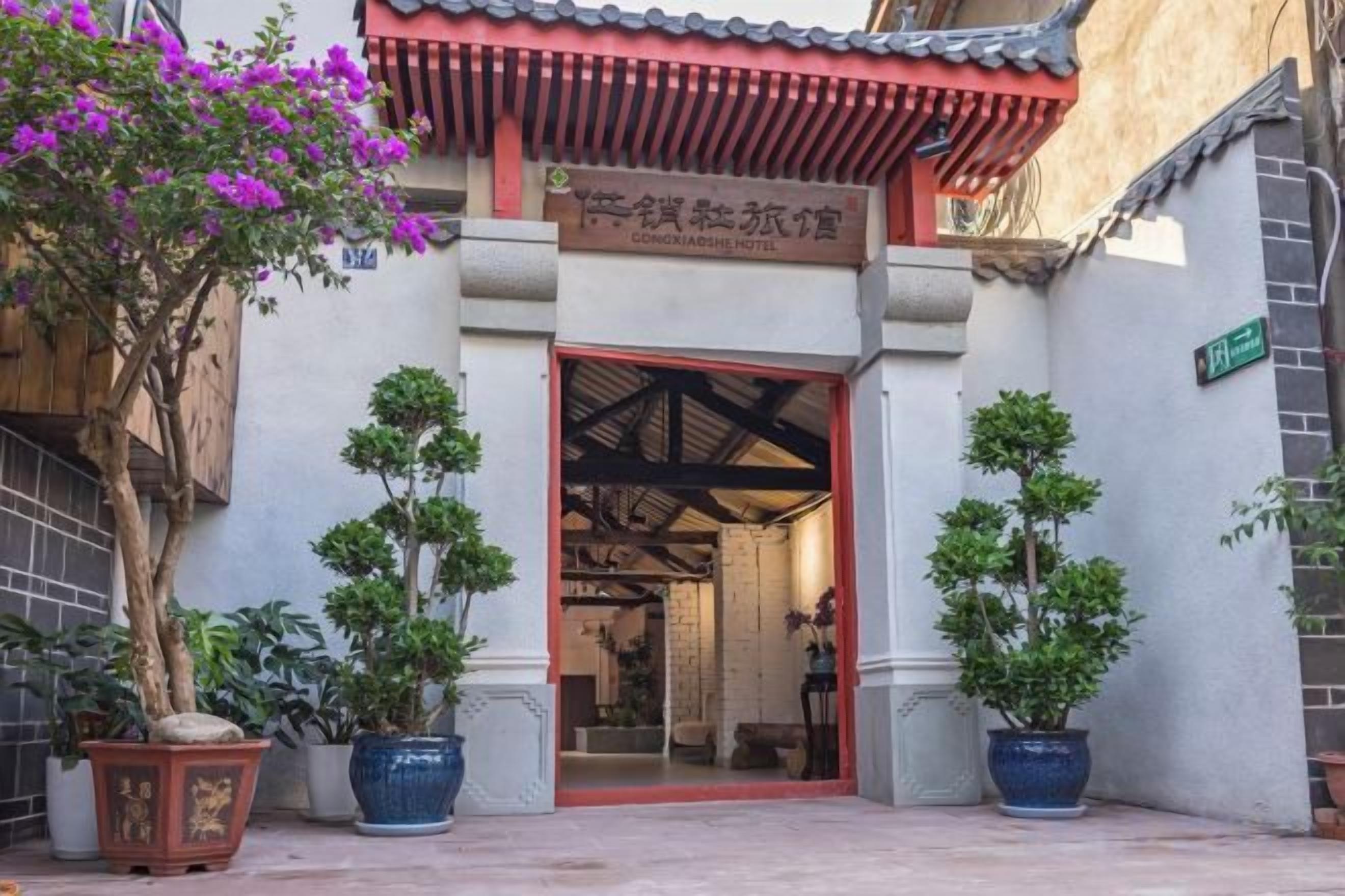 Un edificio tradicional con tejado rojo y un letrero que indica un hotel. Hay plantas en macetas frente a la entrada.