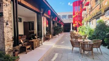 Un espacio al aire libre con mesas y sillas, un edificio de ladrillo y faroles rojos.