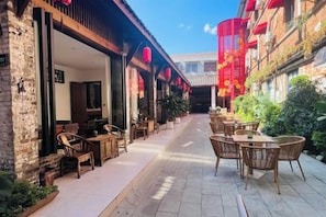 An outdoor seating area with tables and chairs, a brick building, and red lanterns. - Gongxiaoshe Inn (Luo Dai Ancient Town) (Chengdu)