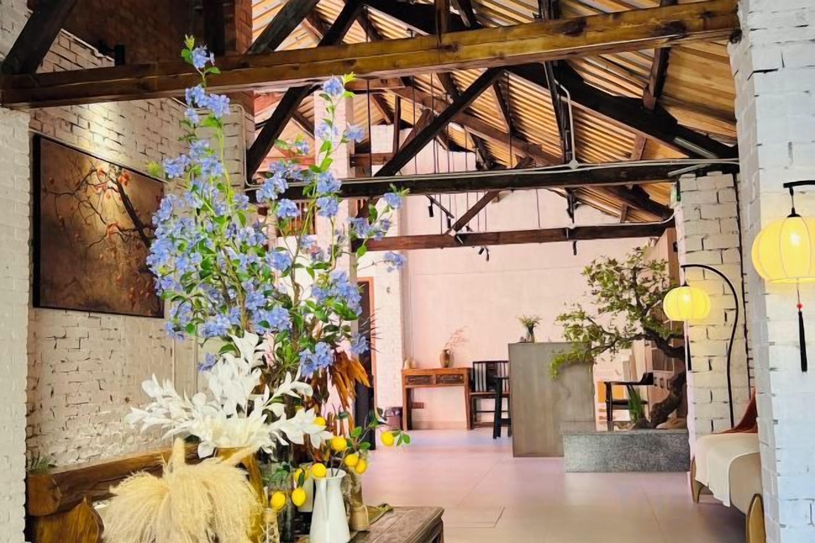A spacious interior with exposed wooden beams, a brick wall, and a seating area with a floral arrangement.