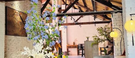 A spacious interior with exposed wooden beams, a brick wall, and a seating area with a floral arrangement.