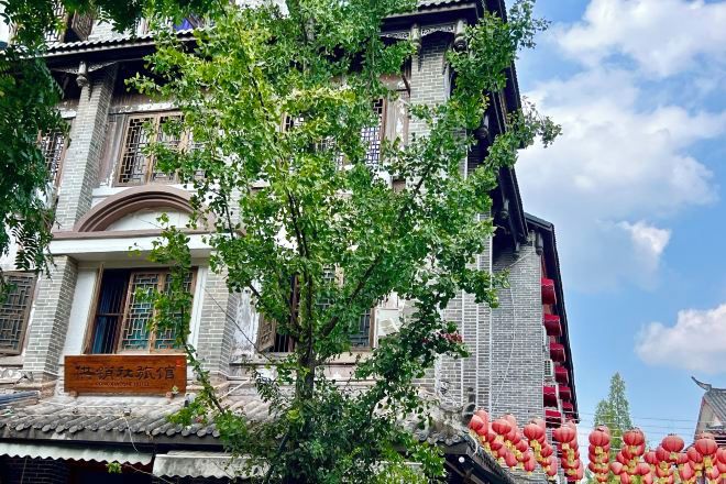 A traditional building with a tiled roof, a visible entrance, and a tree in front.