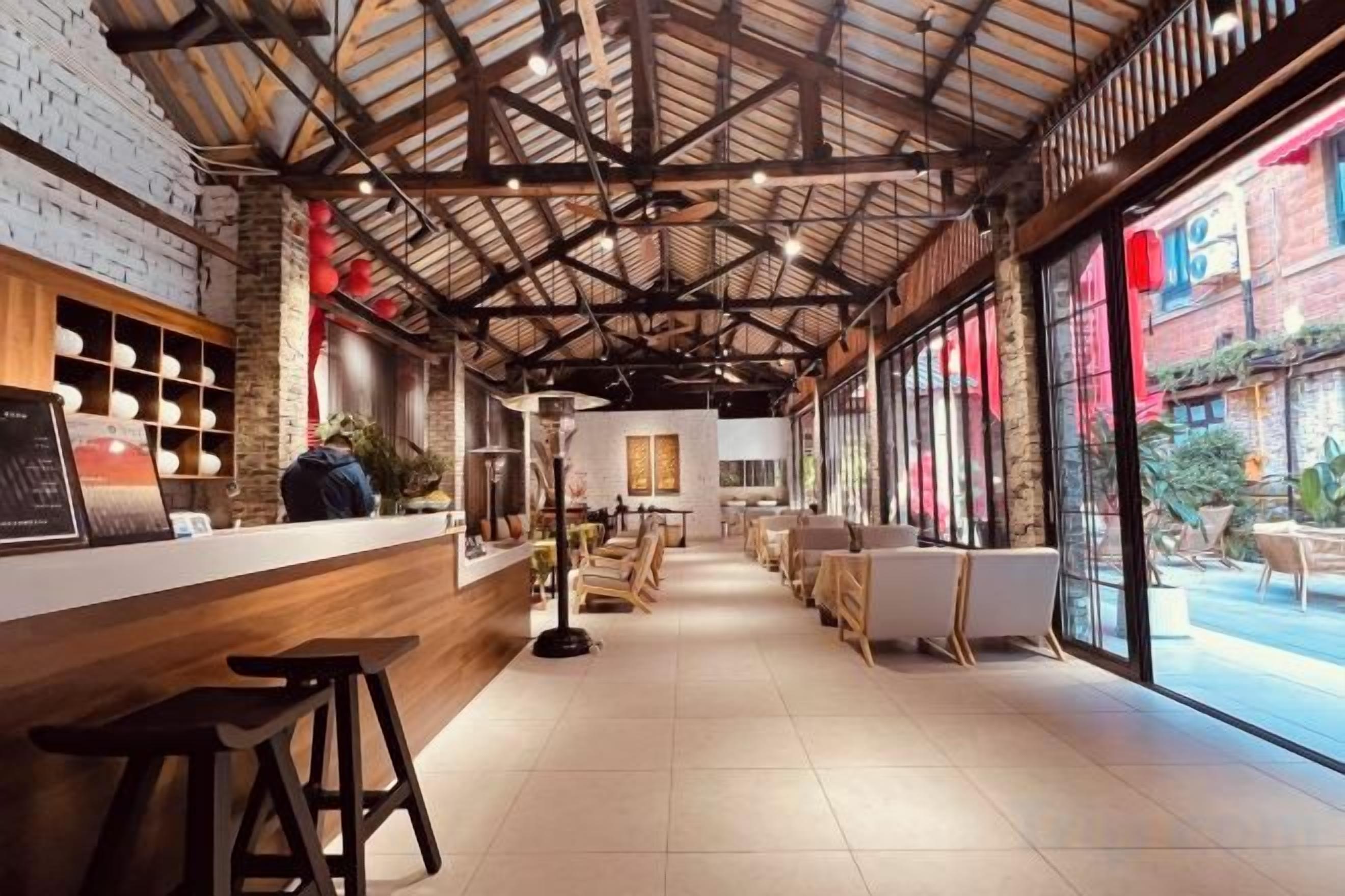 Interior de un restaurante con mostrador de madera, taburetes de bar y vista a la calle a través de amplios ventanales.