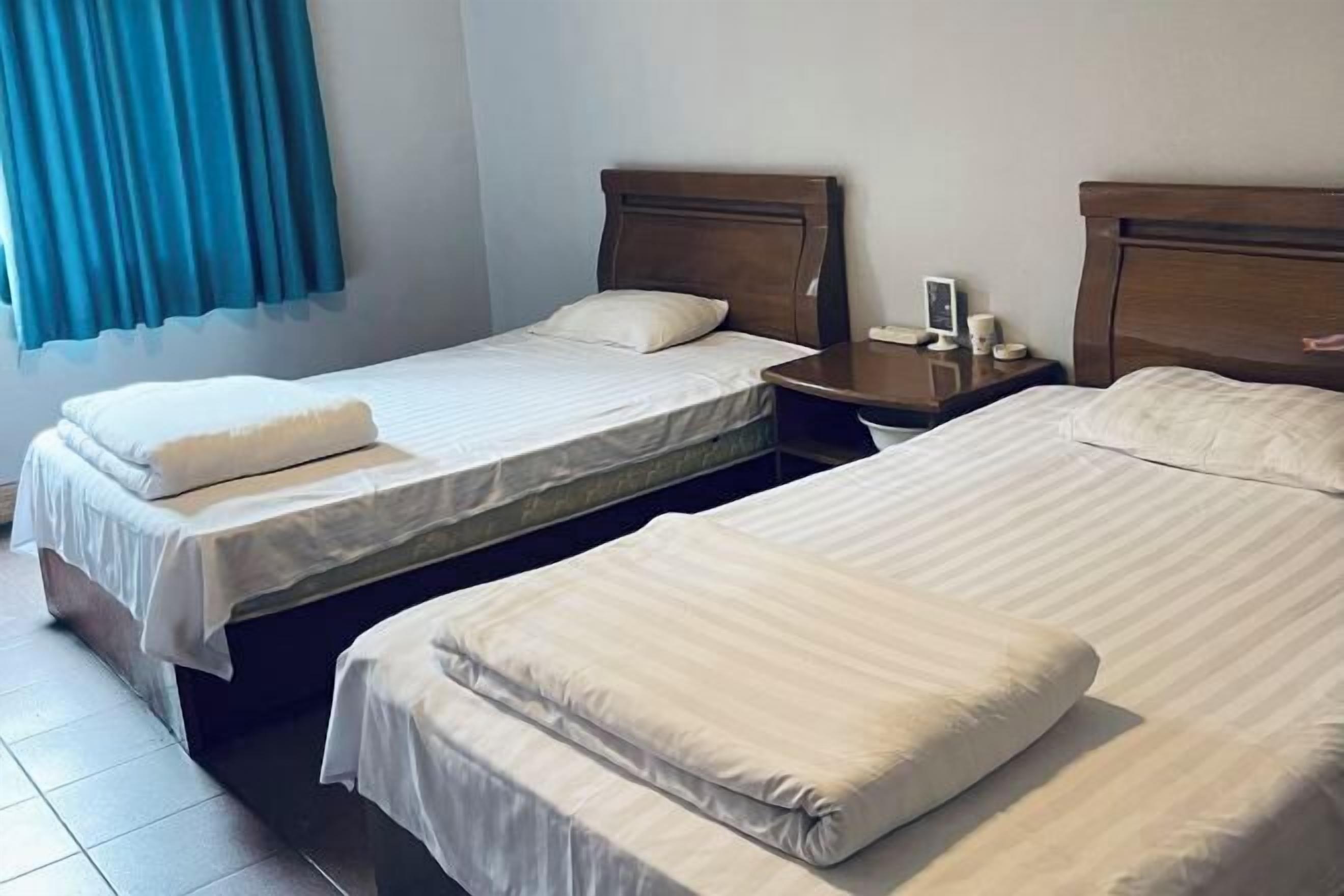 Habitación de hotel con dos camas individuales, una mesita de noche con lámpara y una ventana con cortinas.