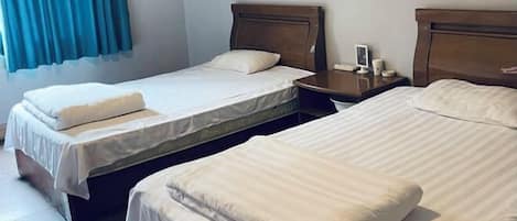 Habitación de hotel con dos camas individuales, una mesita de noche con lámpara y una ventana con cortinas.
