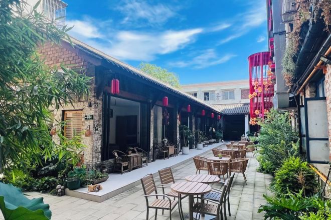 An outdoor dining area with tables and chairs, a brick building, and a red decorative structure.