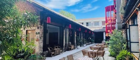 Un área de comedor al aire libre con mesas y sillas, un edificio de ladrillo y una estructura decorativa roja.