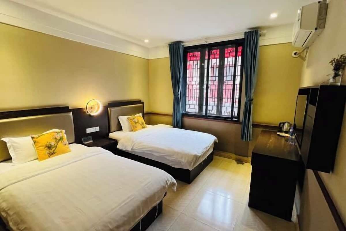 A hotel room with two beds, a desk, a TV, and a window with curtains.