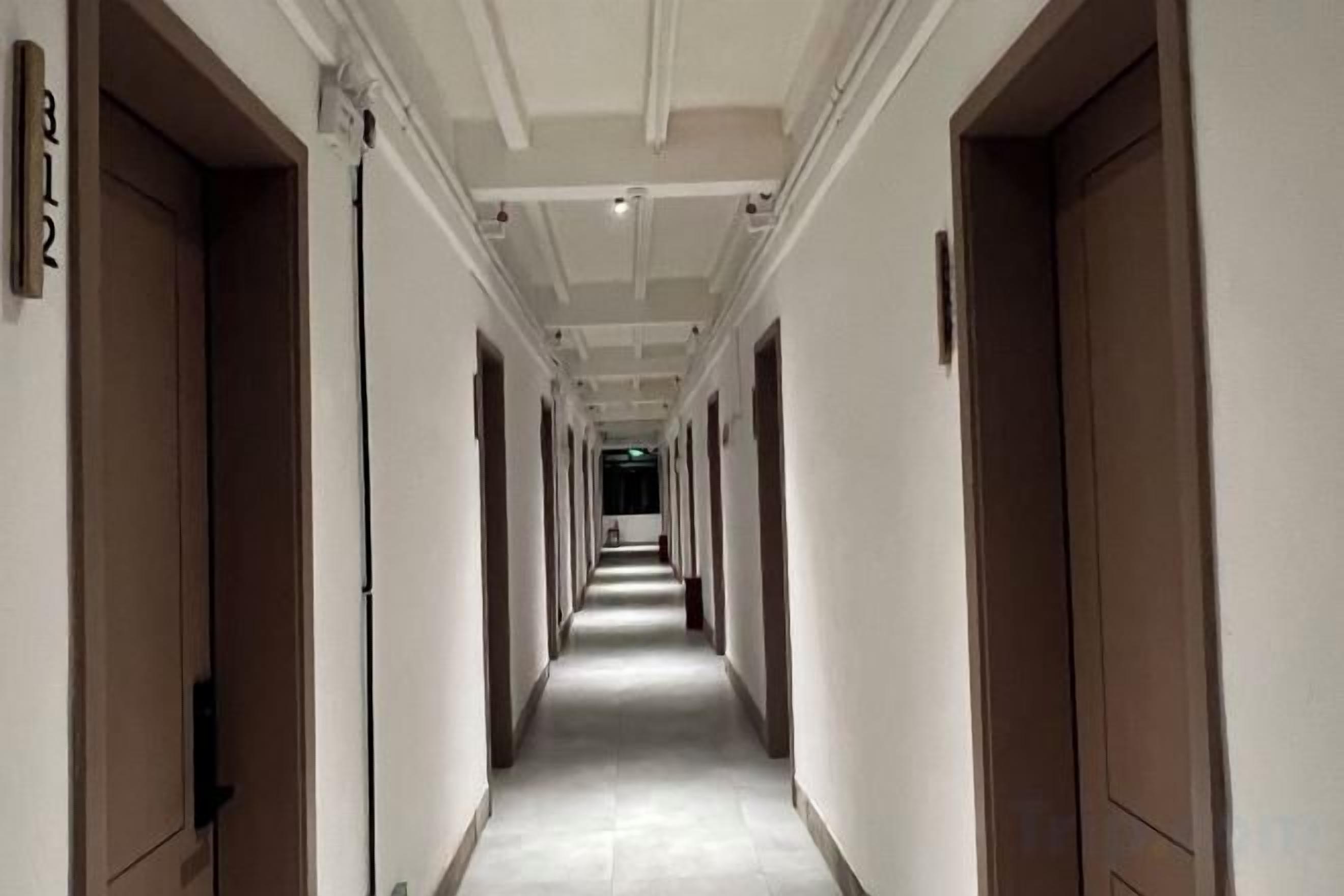 Un largo y estrecho pasillo de hotel con puertas a ambos lados, que conduce a habitaciones individuales.