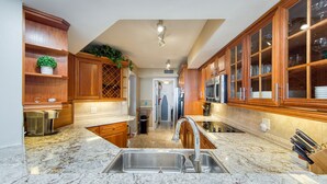 A kitchen with wooden cabinets, a stainless steel sink, and a marble countertop. - Paradise Penthouse (St. Petersburg)
