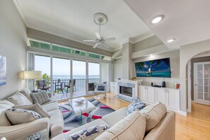 Een ruime woonkamer met een grote bank, een salontafel en een open haard. Er is een balkon met uitzicht op de oceaan.