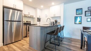 Une cuisine moderne dotée d’appareils électroménagers en acier inoxydable, d’un îlot central avec des tabourets de bar et d’un coin repas avec une table et des chaises en bois foncé.