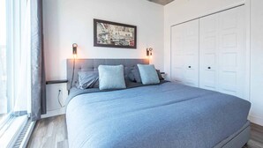 Une chambre à coucher avec un grand lit, deux tables de chevet, une tête de lit, un tableau encadré au mur et une armoire.