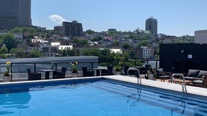 Une piscine sur le toit, agrémentée de chaises longues et de tables, et entourée d’immeubles.