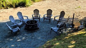 Une terrasse en gravier agrémentée de fauteuils Adirondack disposés autour d’un foyer central.