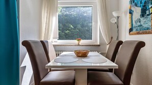 A dining area with a table and chairs, a window with curtains, a radiator, and a wall-mounted lamp.
