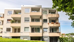 A multi-story residential building with balconies, windows, and a grassy area in front.