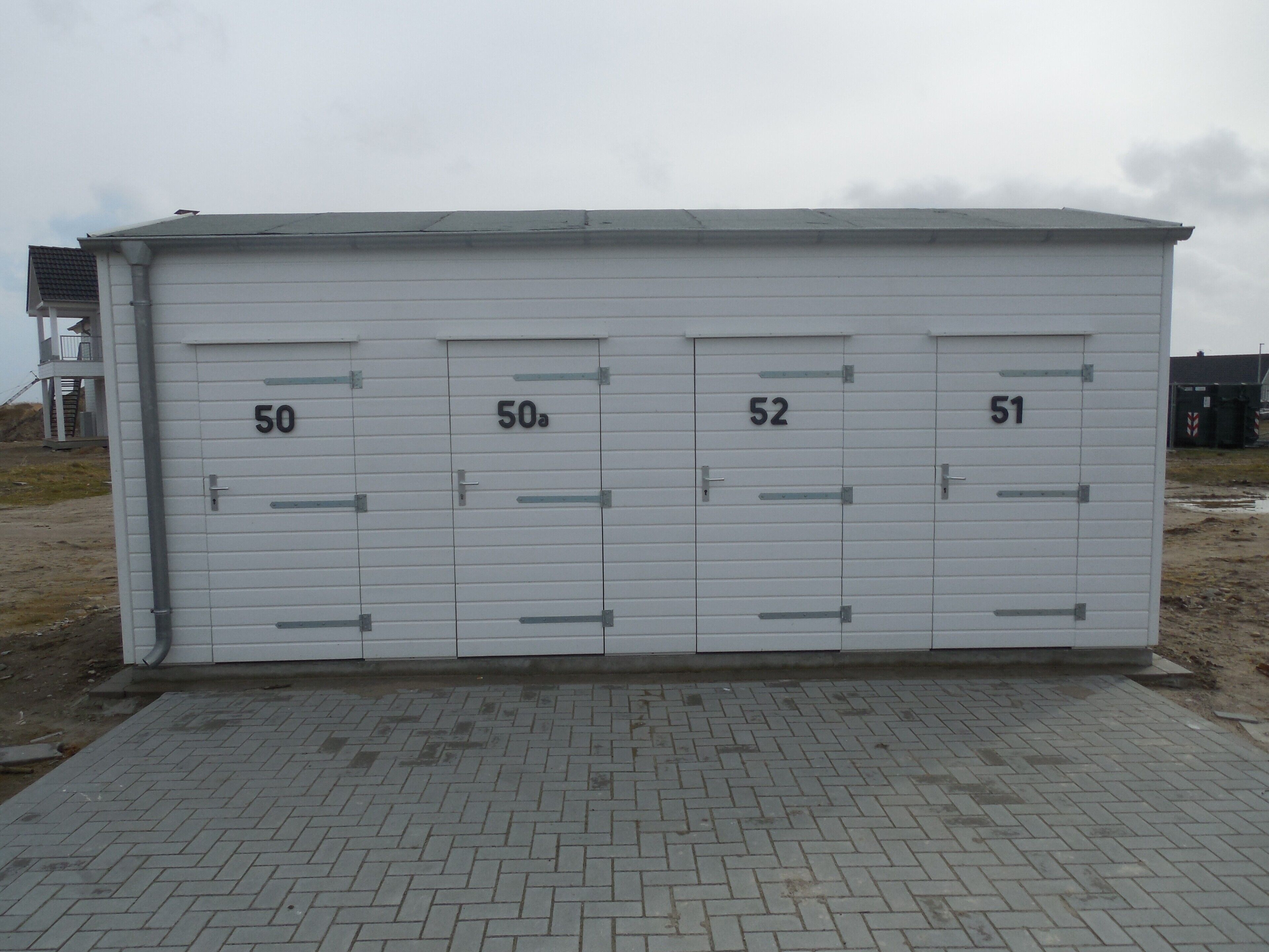 Een gebouw met genummerde deuren, een verharde ingang en een bewolkte lucht.