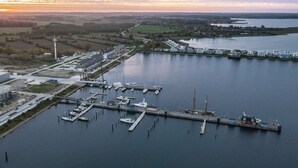 Luchtbeeld van een jachthaven met aangemeerde boten, een vuurtoren en omliggende velden.