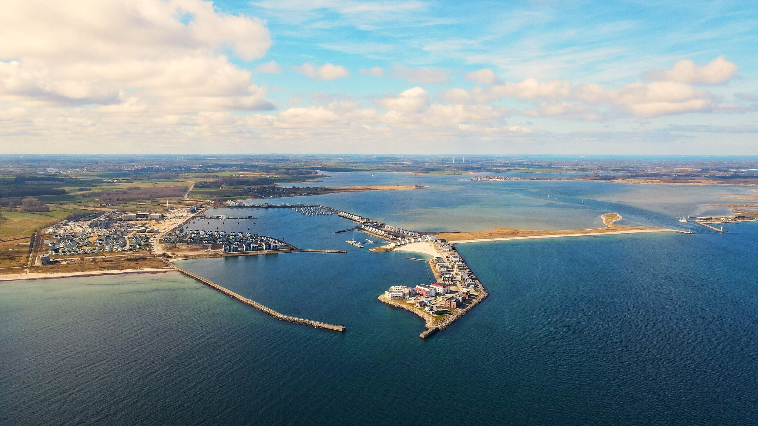 Vista aérea de una zona costera con un puerto deportivo, un muelle y una pequeña isla con edificios.