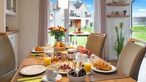 Een ontbijttafel met croissants, fruit en drankjes, met uitzicht op een woonwijk.