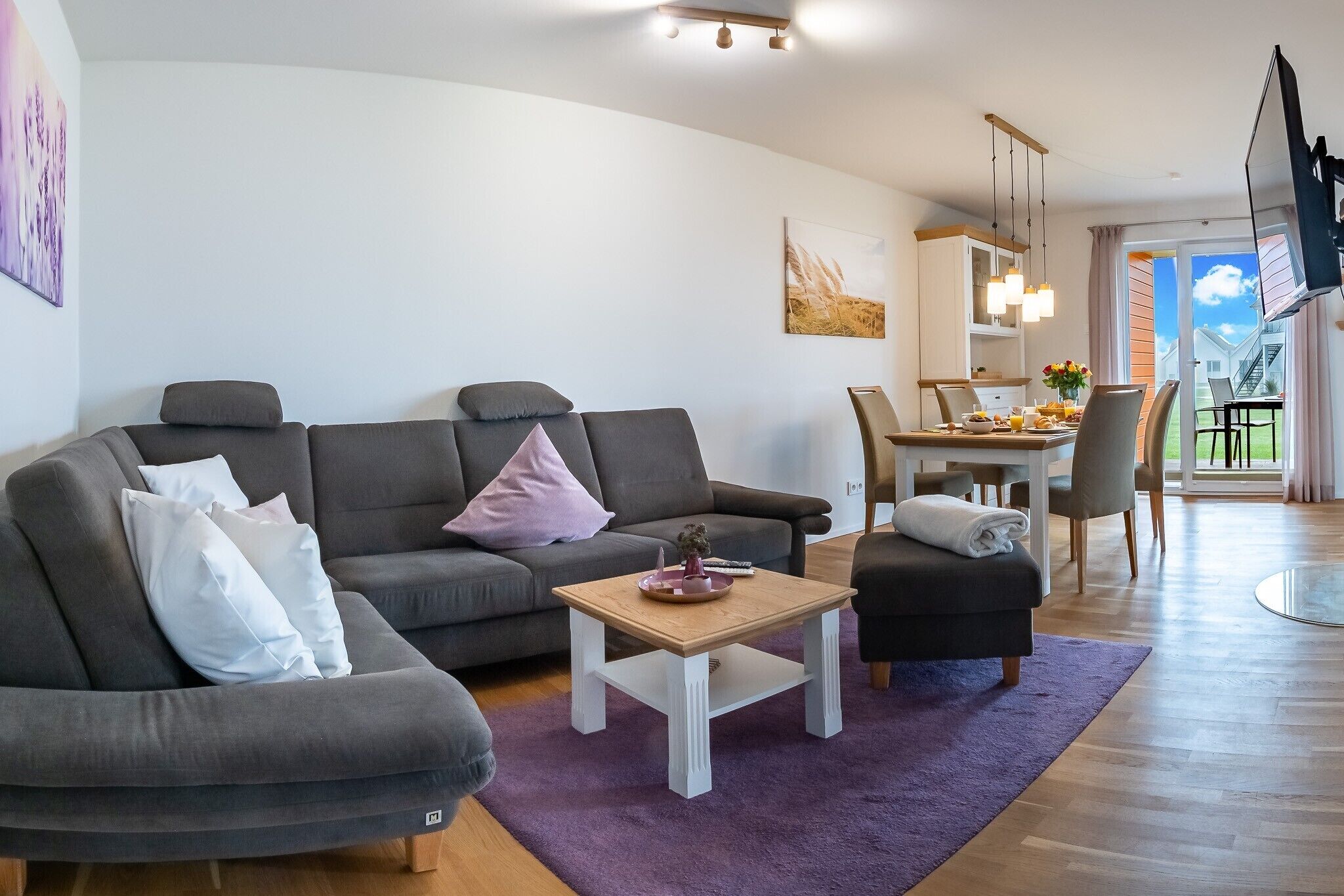 Un salon moderne avec un canapé gris, une petite table en bois et un coin repas comprenant une table et des chaises blanches.