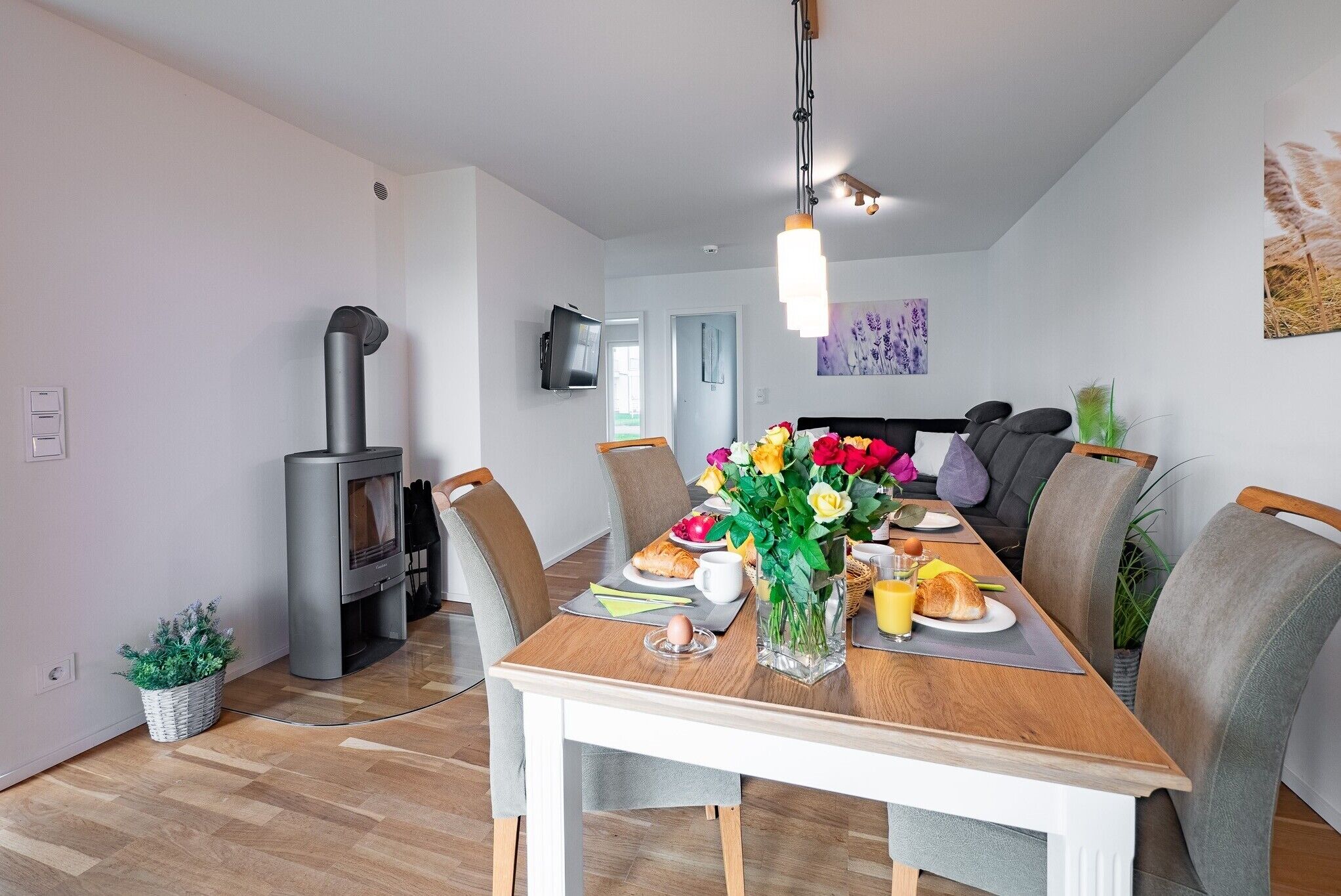 Ein Essbereich mit Holztisch, Stühlen, einem Blumenstrauß und einem an der Wand befestigten Fernseher.