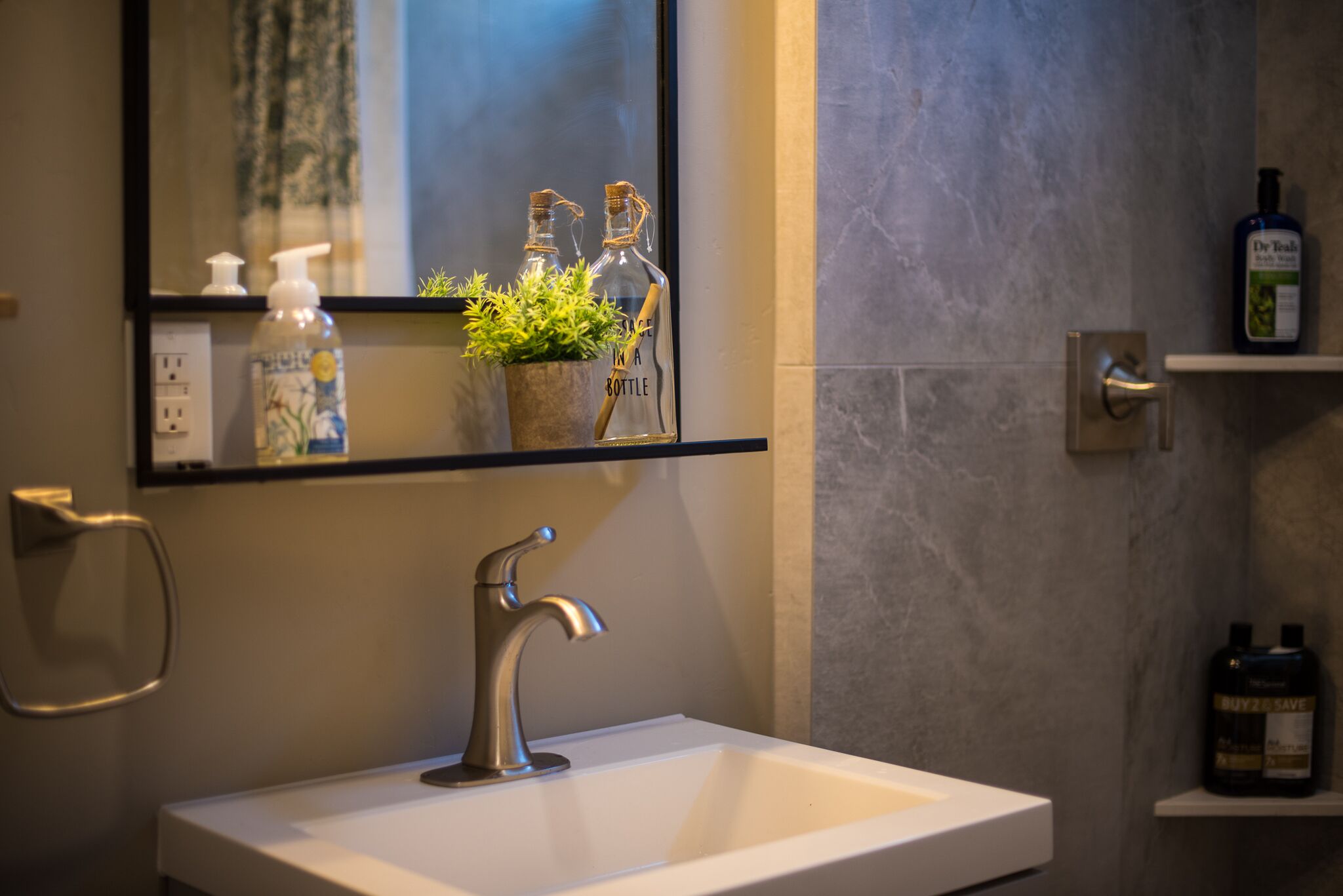 Un baño con un lavabo blanco, un espejo y un estante con artículos de aseo.