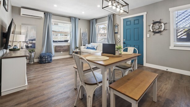 A modern kitchen with a dining area, wooden flooring, and a blue door.