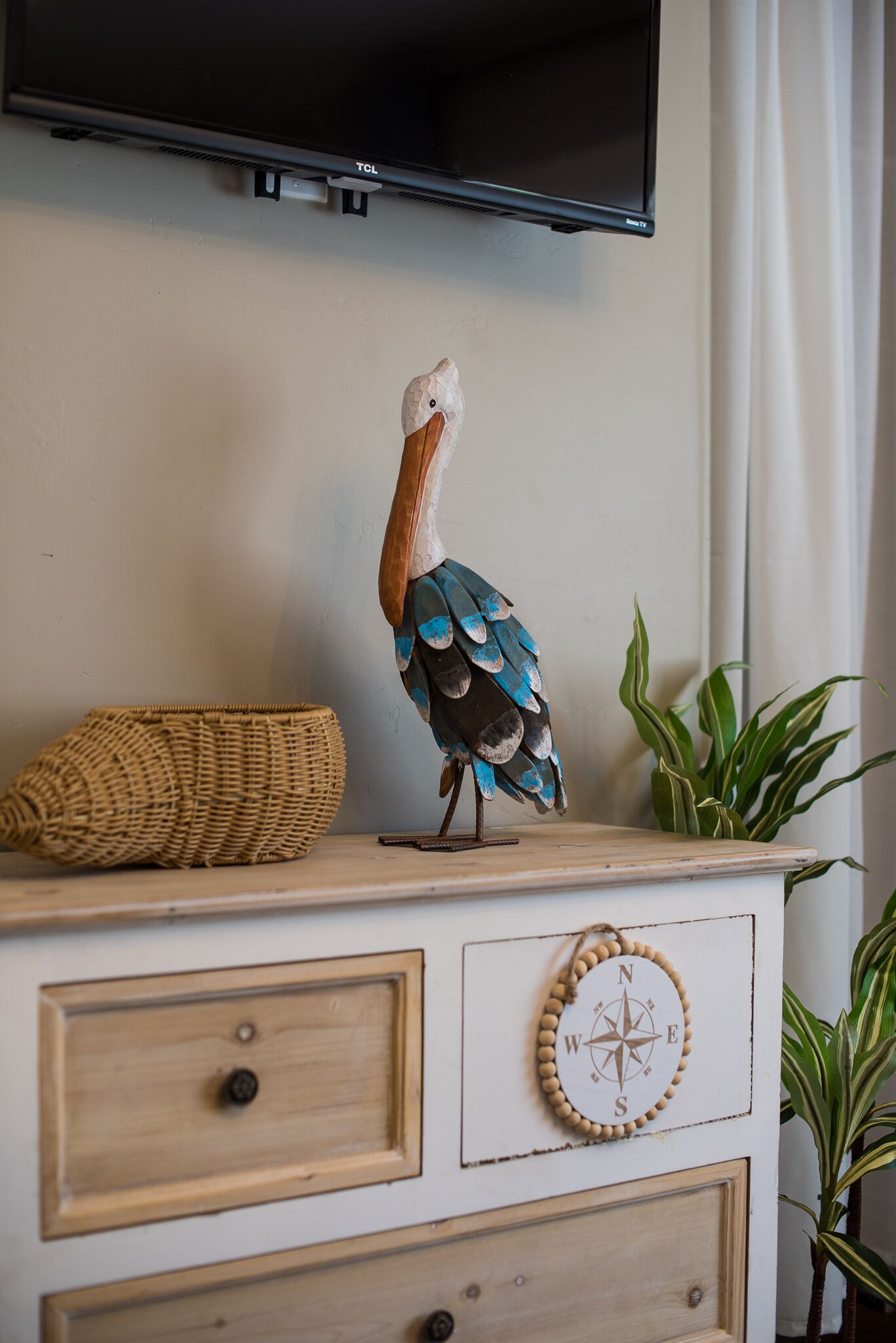 A decorative peacock on a dresser with a compass wall decoration and a woven basket.