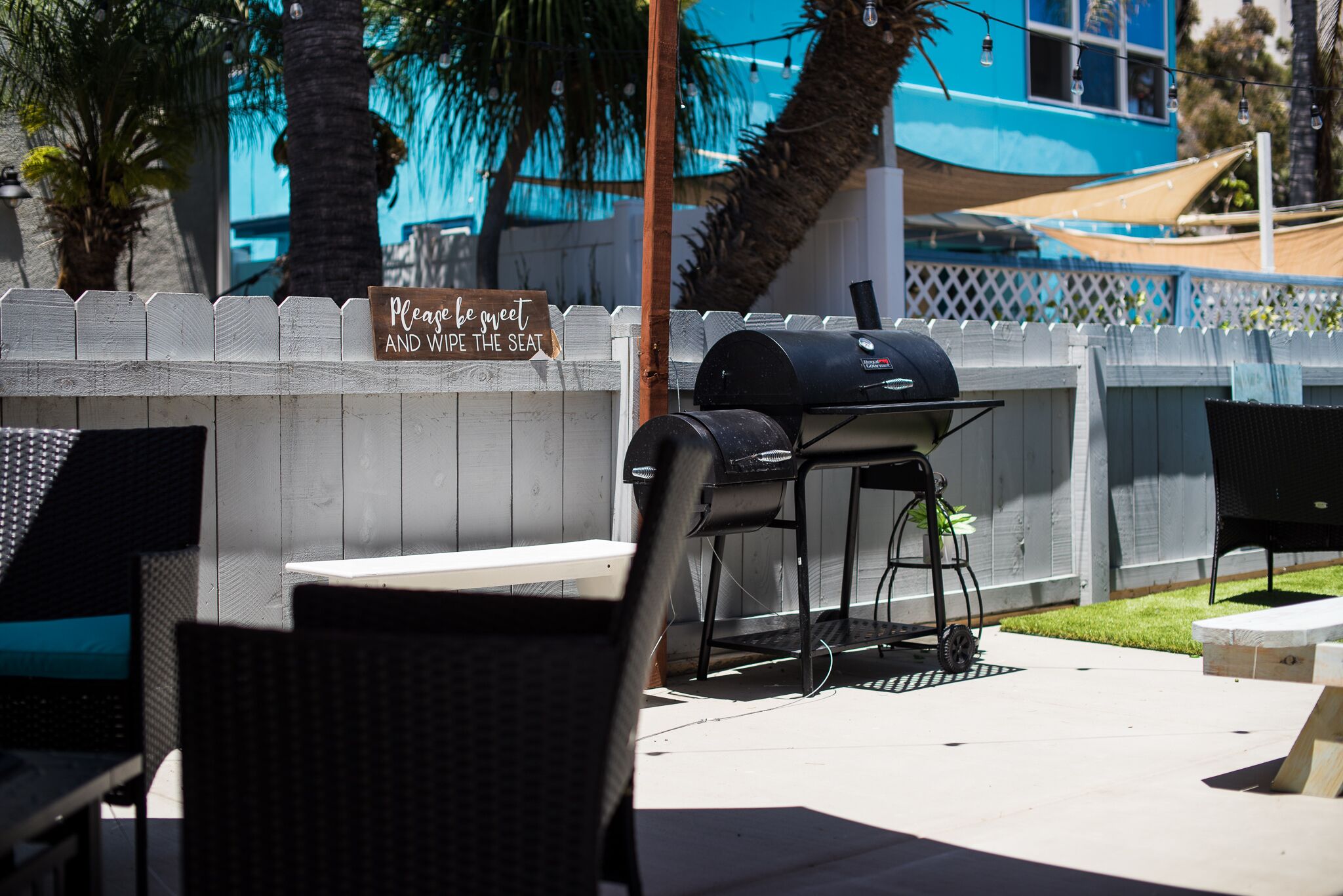 En udendørs terrasse med grill, stole og et skilt der siger "Vær sød at tørre sædet af".