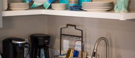 Una cocina con encimera blanca, cafetera, cesta para café y fregadero.