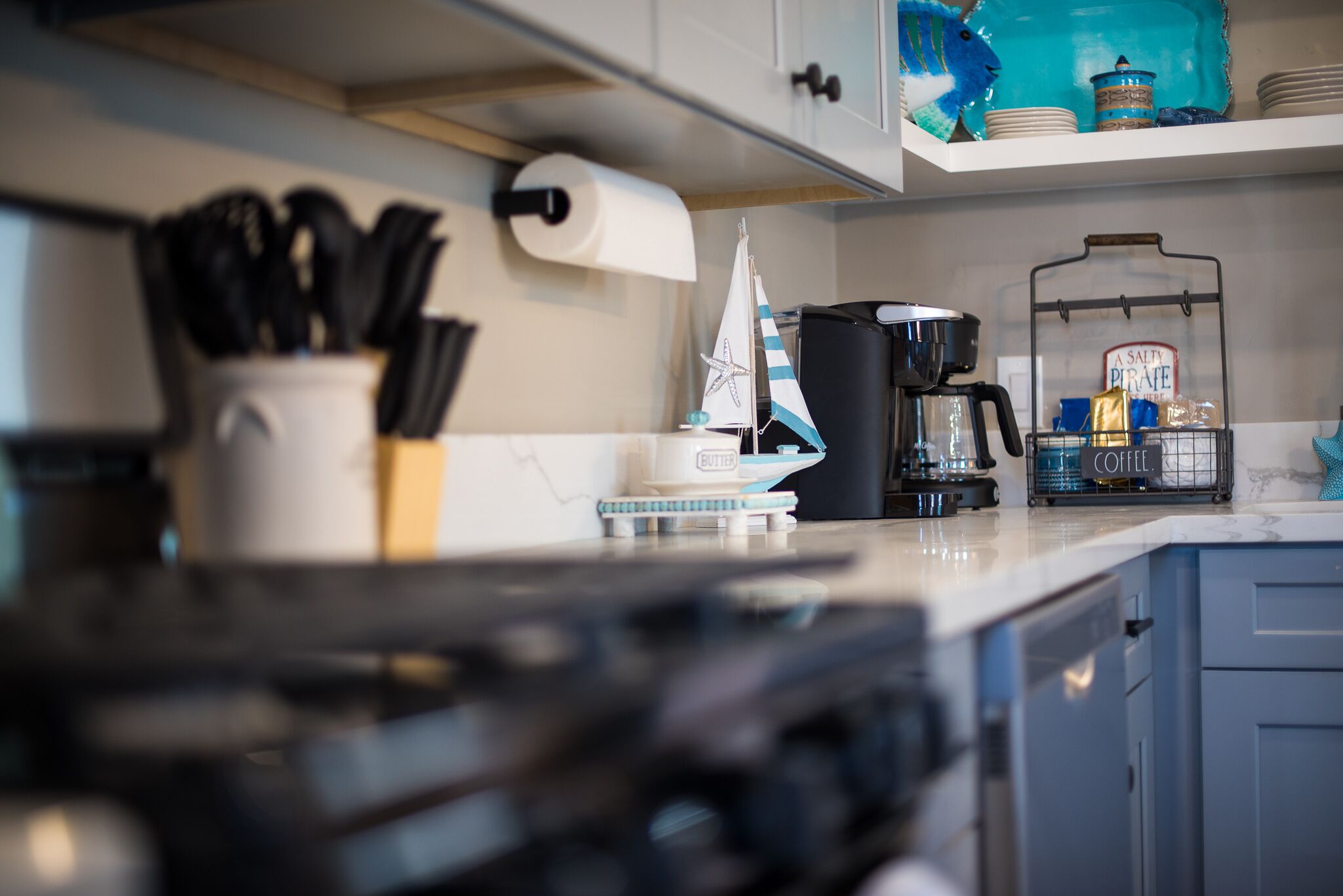 A kitchen with a stove, coffee maker, and a shelf with decorative items.