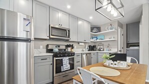 A modern kitchen with stainless steel appliances, white cabinetry, and a wooden dining table.
