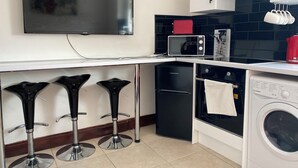 A compact kitchen with a flat-screen TV, a microwave, a small refrigerator, a washing machine, and three bar stools. - 2 Bed Flat - Sleeps 6 - Parking - Wifi (Swansea)