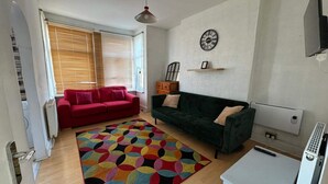 A living room with a red and green sofa, a colorful rug, a wall clock, and a TV. - Newport Cozy Apartment Retreat (Newport)