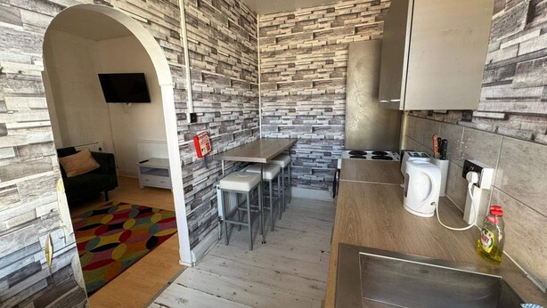 A compact kitchen with a stone-patterned backsplash, a dining area with a small table and chairs, and a built-in stove. - Newport Cozy Apartment Retreat (Newport)