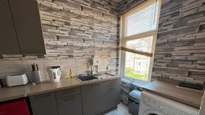 A kitchen with a stone wall backsplash, a window, a washing machine, and a red cabinet. - Newport Cozy Apartment Retreat (Newport)