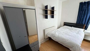 A bedroom with a bed, a wardrobe, a radiator, and a window with curtains. - Newport Cozy Apartment Retreat (Newport)
