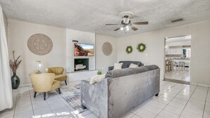 Una sala de estar con un sofá gris, un sillón amarillo, una chimenea y un ventilador de techo.
