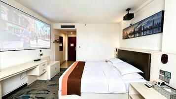 A hotel room with a bed, a desk, a TV, and a cityscape painting.