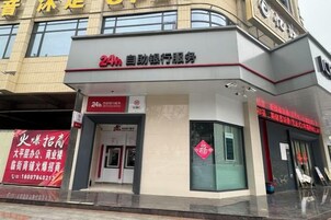 Un edificio con un letrero que indica servicio las 24 horas, una entrada visible y un cartel rojo a la izquierda.
