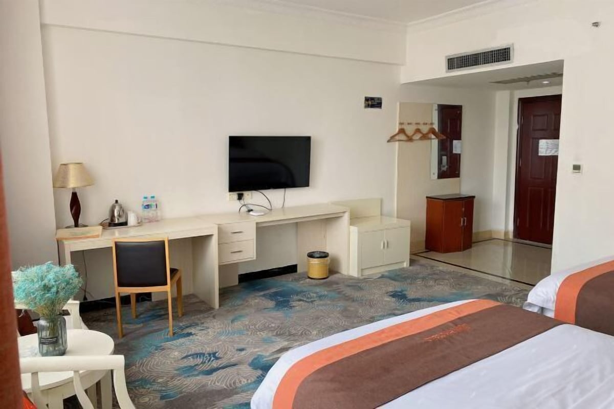 Quarto de hotel com cama, escrivaninha, televisão, espelho e guarda-roupa.