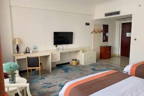 Quarto de hotel com cama, escrivaninha, televisão, espelho e guarda-roupa.