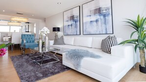 En moderne stue med en hvid sofa, et glasbord og abstrakt kunst på væggen.